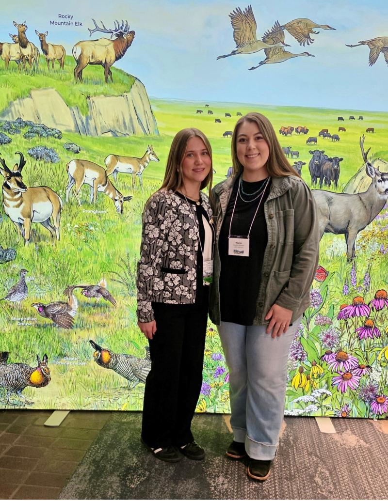 Two females smile for the camera in front of a painted range backdrop