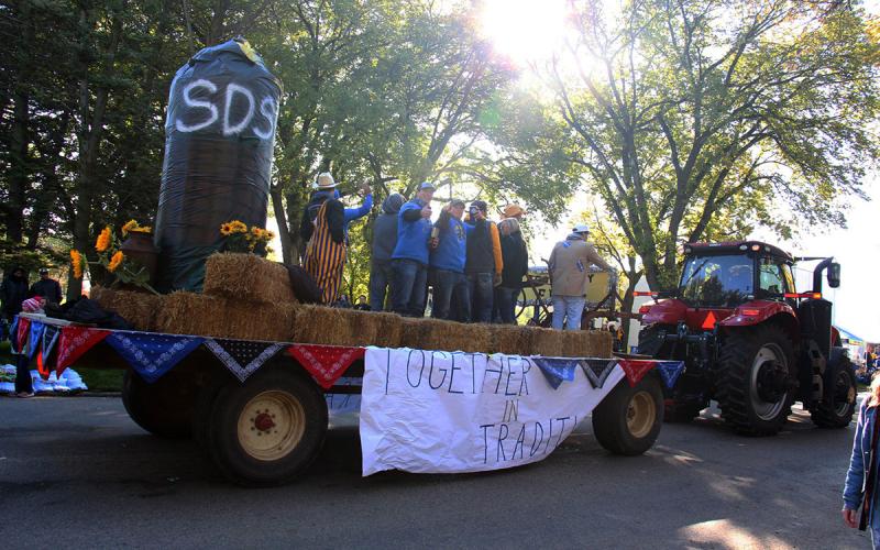 Tractor pulling an agriculture-themed float during a fall parade.