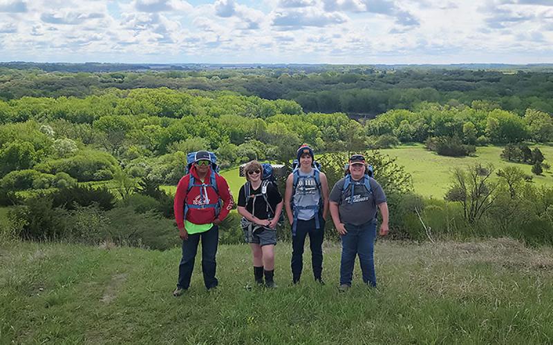 Group of youth with hiking gear standing atop a hill.