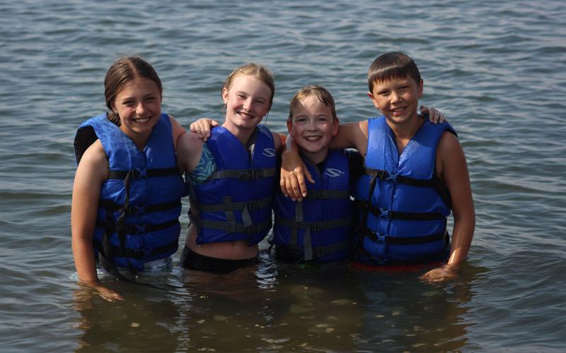 Children wearing life jackets while swimming in a lake.
