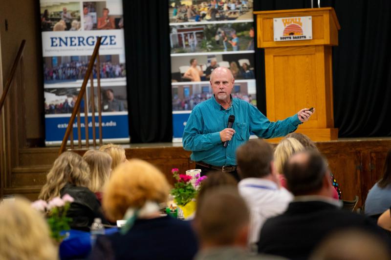 A man holding a microphone speaks to a room of people