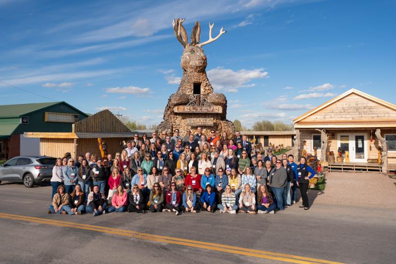 A group of people smiles underneath a huge Jackalope statue