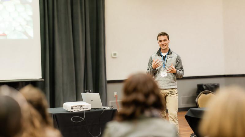 A young man gives a presentation to a room of people