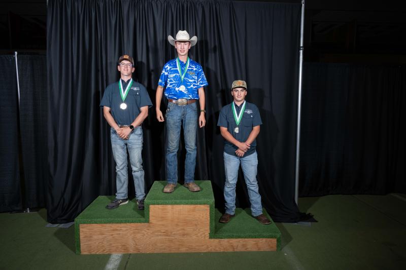 A teenage boy in a blue shirt and white cowboy hat stands in the first-place spot on a podium