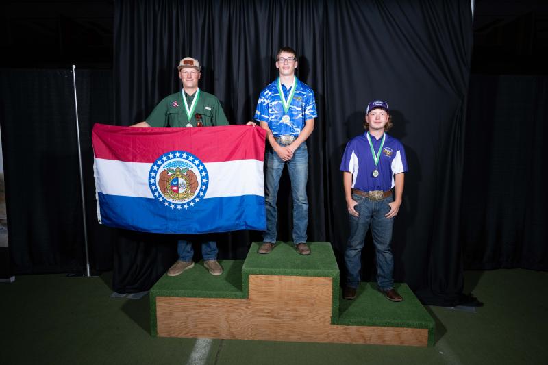 A teenage boy in a blue shirt stands in the first-place spot on a winners podium