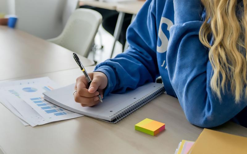 Young woman sitting at a desk with financial documents, a notebook, folders, and colored post-it notes.