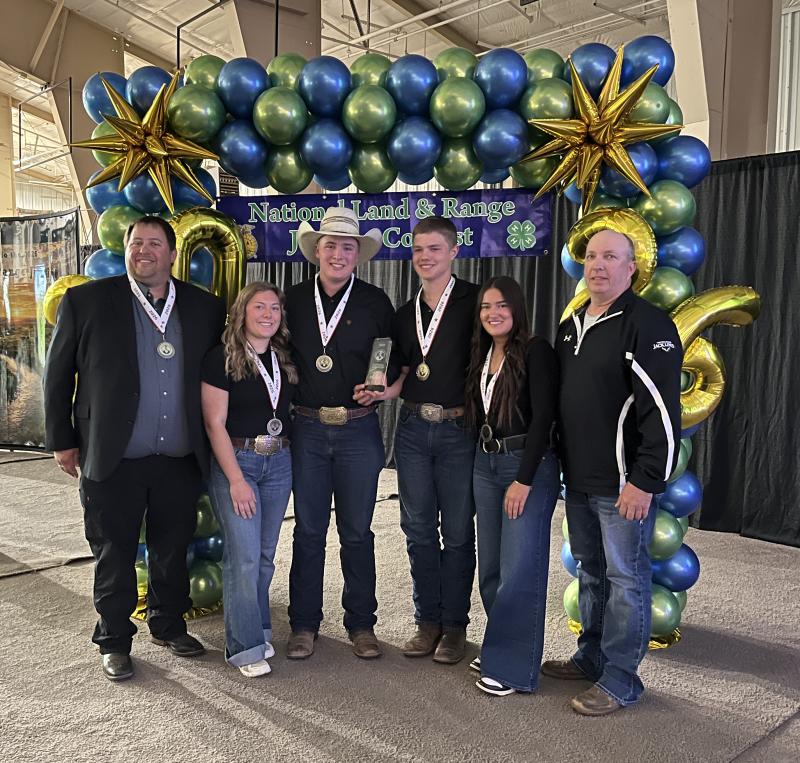 Six people smile wearing medals and holding first-place award plaques