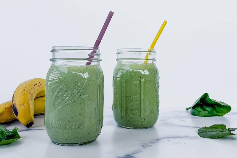 Two mason jars with fruit and vegetable smoothies in them on a marble countertop.