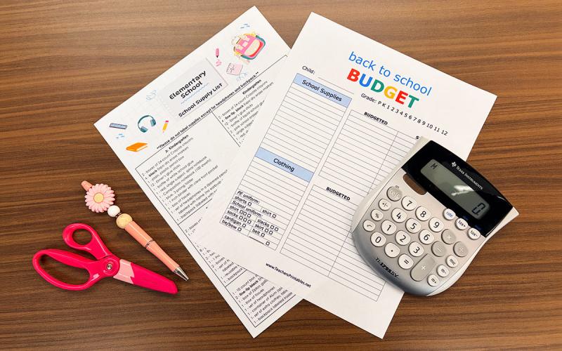 Schools supply list, budget sheet, pen, scissors, and calculator arranged on a tabletop.