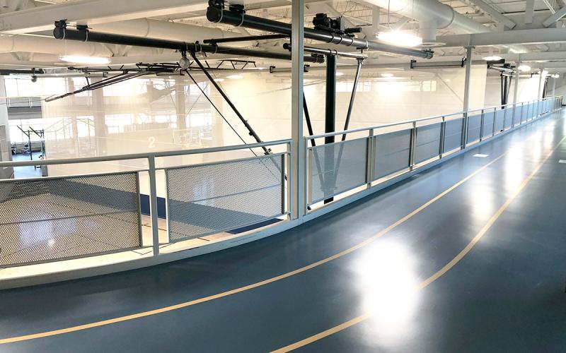 Second-level indoor track overlooking a series of basketball and volleyball practice courts.