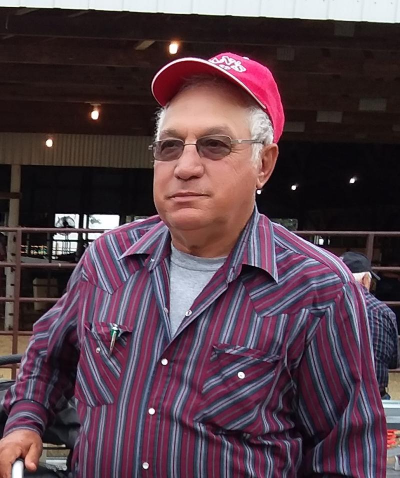 A man wearing a red baseball cap, sunglasses and purple striped button-up shirt poses for a photo