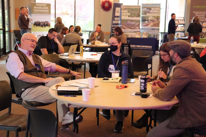 People sit at round tables with coffee cups and open notebooks