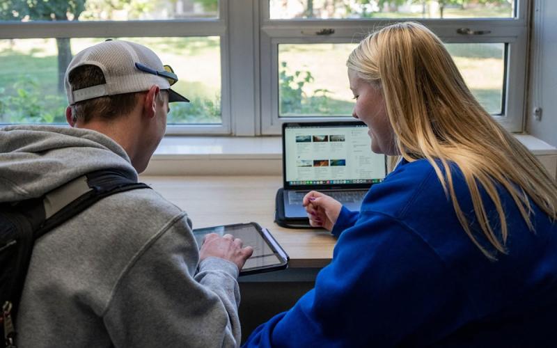 Young man and woman reviewing information on a tablet and laptop computer.