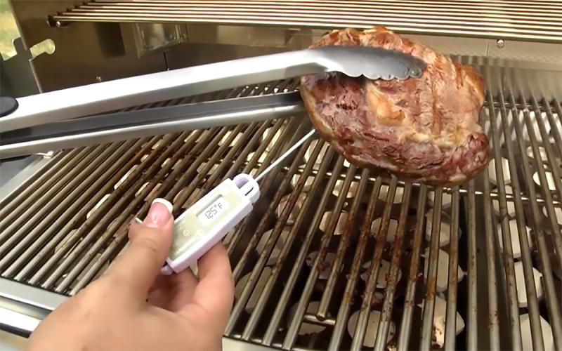 Hands checking internal cooking temperature of a beef steak using a food thermometer.
