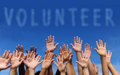 many hands raised in the air with sky background and the word volunteer