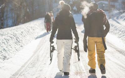 Two young women wearing layers of winter clothing walking down a snowy road