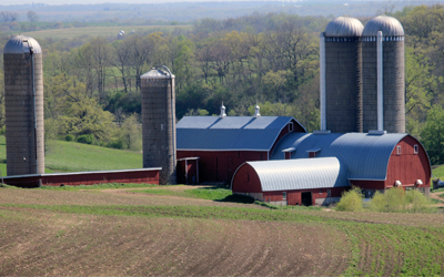 A series of red barns and grain silos on rolling hills in a farmyard.