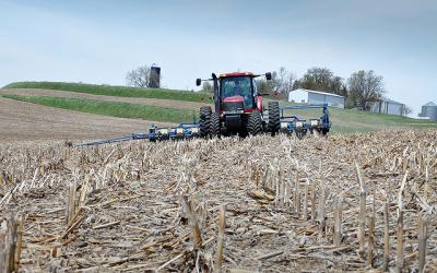 A red tractor and seed drill planting in a no-till field.