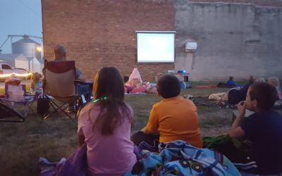 A group of people watching a movie outdoors on a video screen on the side of a brick building.