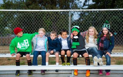 Character Links 5 Curriculum Diverse group of school-age children sitting on bleachers outside in 4-H clothing.; Photos; 4-H Grows Here; Brand; 4-H youth
