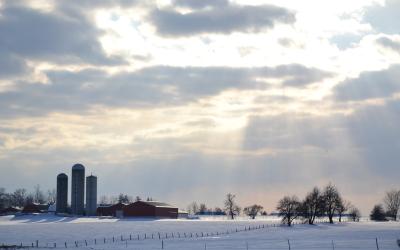 A snowy farmyard with sunlight breaking through the clouds.