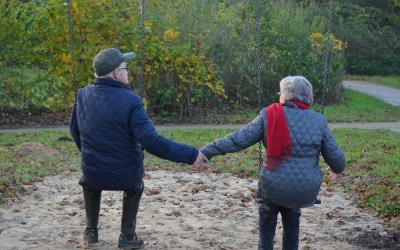An older couple sitting on a swingset holding hands.