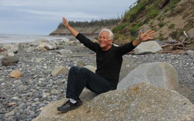 A happy, older adult sitting on a rock by the seashore.