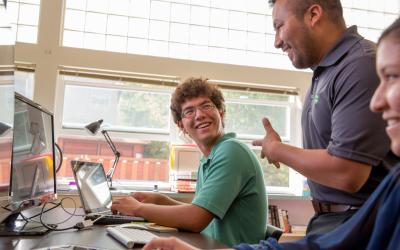 A young man sitting at a laptop discussing a project with a 4-H leader.