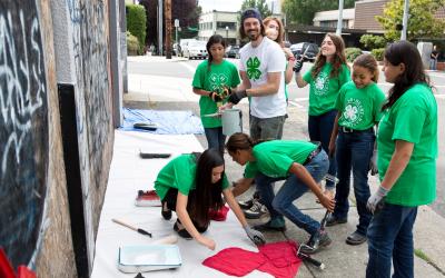a small group of 4-H youth painting over graffiti with their 4-H youth advisor. Photo courtesy of National 4-H.