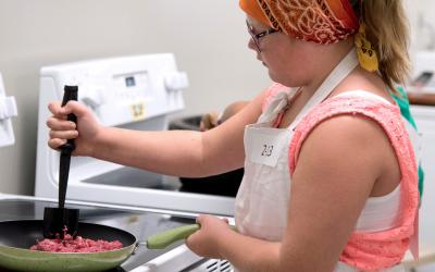 female youth cooking ground beef in a frying pan