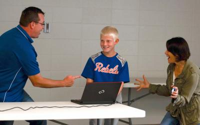 male 4-h youth in a baseball uniform standing between an adult male and female during a presentation