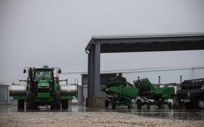 green tractor next to a machine shed with farm equipment inside it