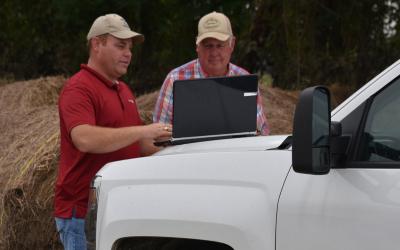 two men viewing a laptop on the hood of a white pickup