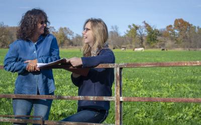 femal rancher with young female training reviewing paperwork beside a cow pasture