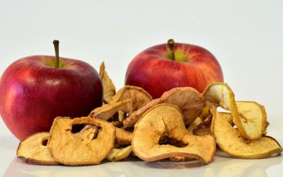 two whole apples behind a small pile of dehydrated apple slices