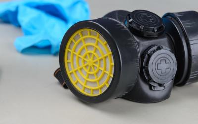 a black and yellow respirator mask with blue protective gloves in the background.