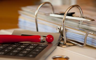 A pen and calculator sitting next to an accounting binder.