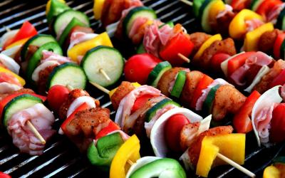 Several kabobs with pieces of fresh vegetables and lean meats cooking on a grill.