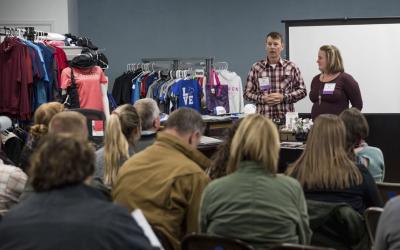 Male and female business owner leading a breakout session to a group of conference attendees inside a small business.