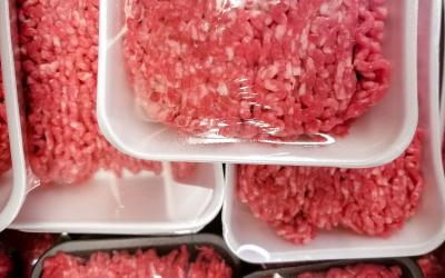 Sealed packages of ground beef stacked inside a meat cooler at a grocery store.