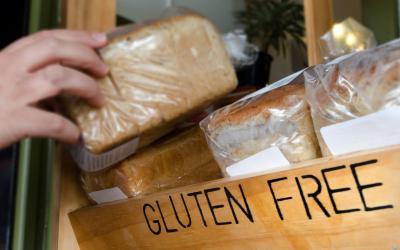 A hand grabbing a loaf of bread from a shelf labeled "gluten-free"