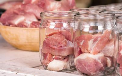 A bowl of raw meat being distributed into clear, glass jars.