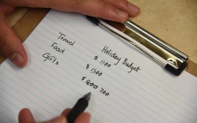 Hands writing out a holiday budget on a notepad.