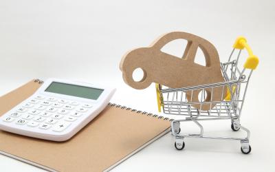 A wooden car cutout placed inside a small shopping cart next to a calculator and a notebook.