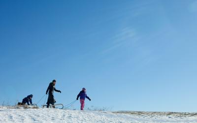 A mother and two daughters pulling sleds through an open field.