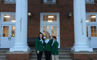 Three women in green jackets standing in front of a building