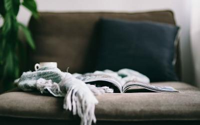 A blanket, book and cup of hot tea arranged on a sofa.