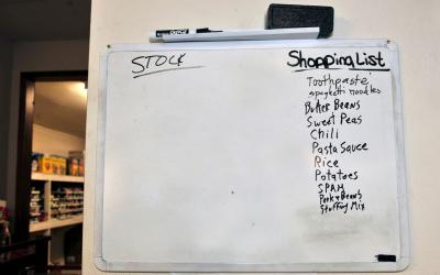 A whiteboard outside a home pantry with a shopping list and a stock list.