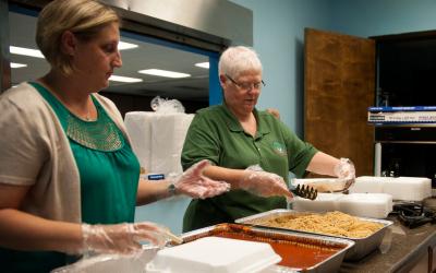 Two women preparing take-out containers for drive-up meal service.