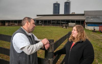 An dairy farmer and site inspector talking near a fence outside a dairy dairy barn.
